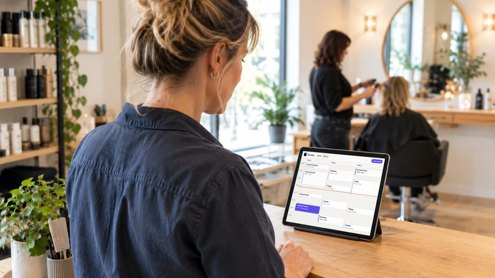 Eine Salon-Inhaberin sieht am Tresen auf dem Tablet die Termine des Tages, ein neuer Online-Termin ist hervorgehoben. Symbolbild, KI-erzeugt.