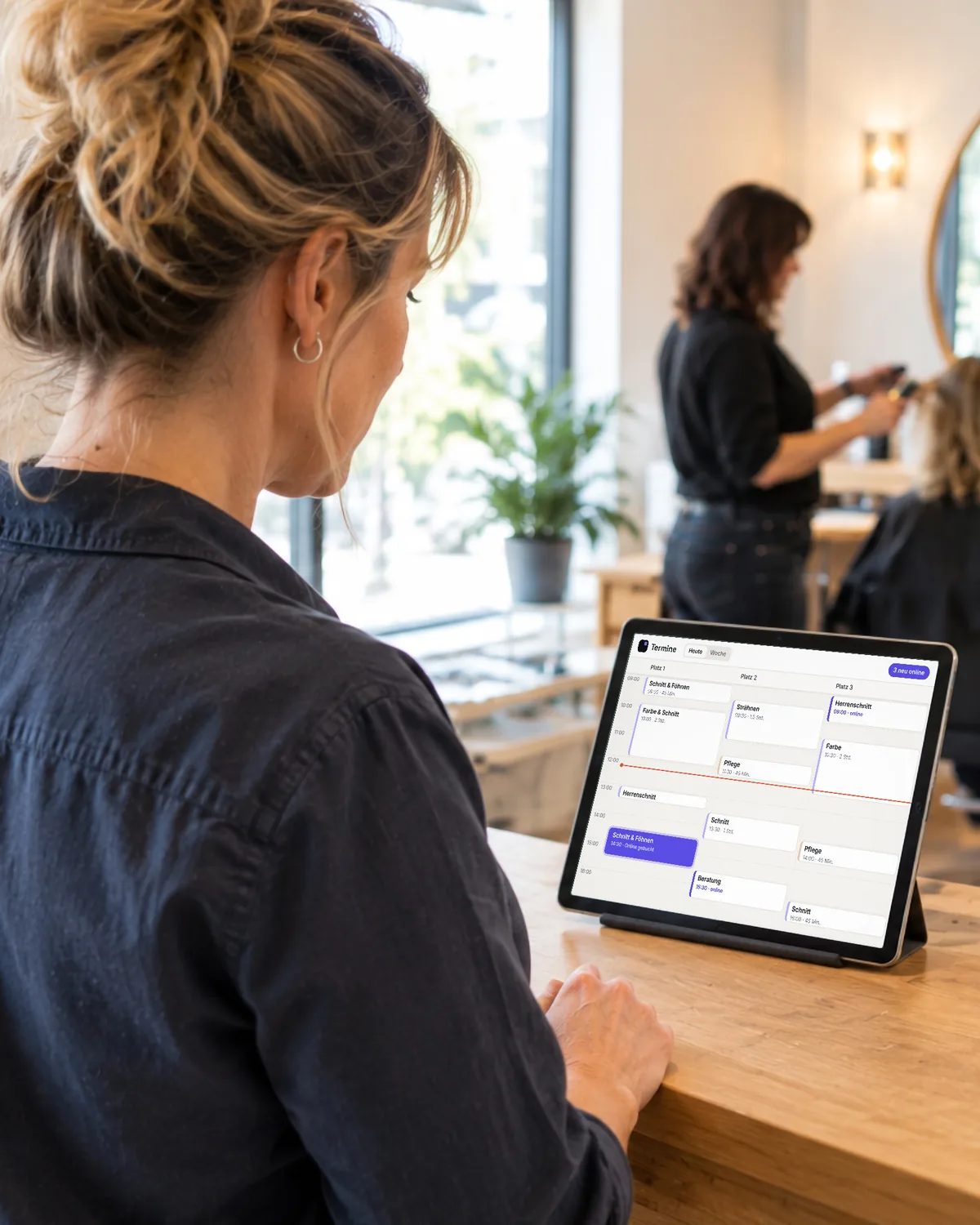 Eine Salon-Inhaberin sieht am Tresen auf dem Tablet die Termine des Tages, ein neuer Online-Termin ist hervorgehoben. Symbolbild, KI-erzeugt.