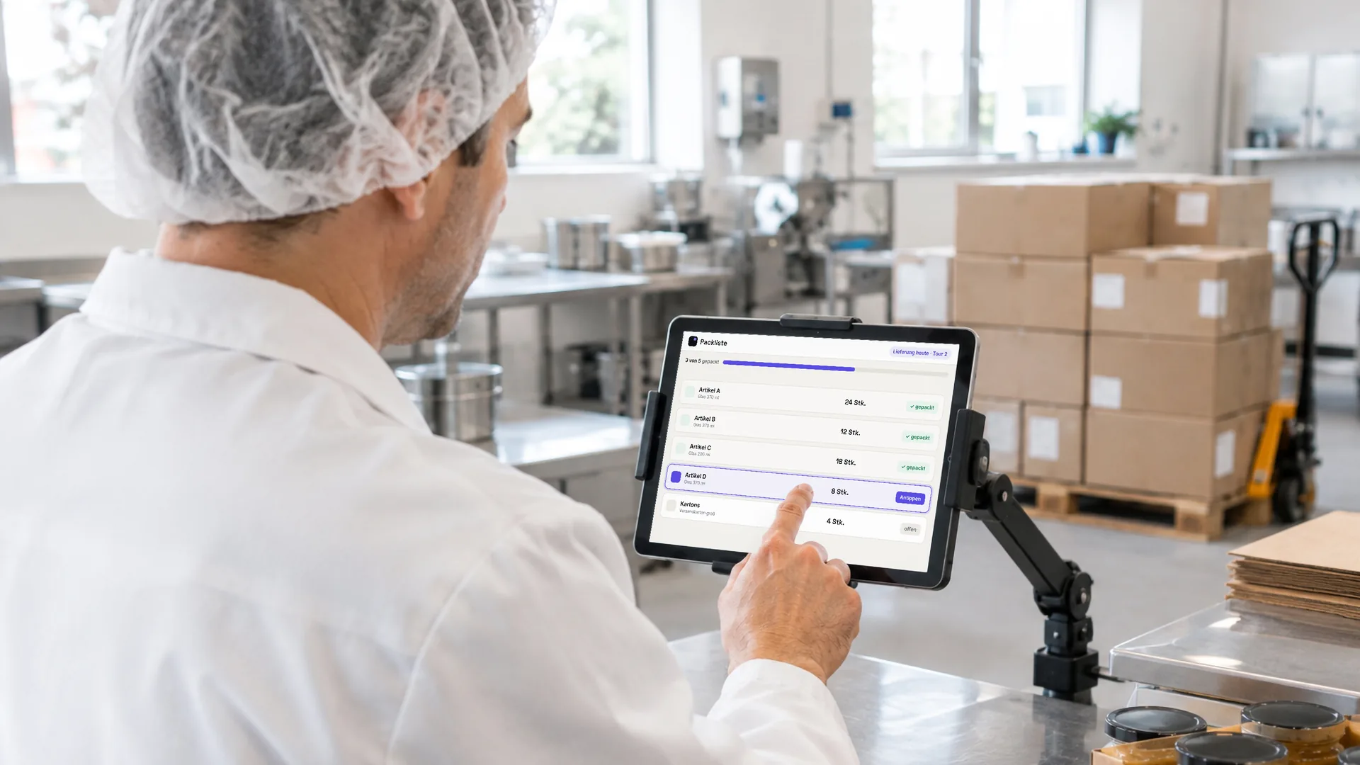 Ein Mitarbeiter einer kleinen Lebensmittelproduktion hakt am Packtisch auf dem Tablet die Packliste für die Lieferung ab. Symbolbild, KI-erzeugt.