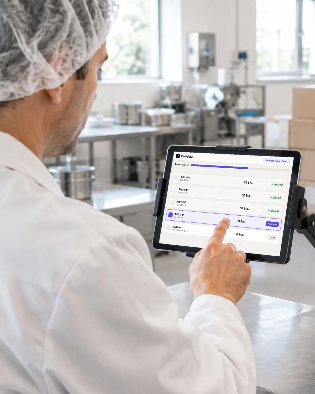 Ein Mitarbeiter einer kleinen Lebensmittelproduktion hakt am Packtisch auf dem Tablet die Packliste für die Lieferung ab. Symbolbild, KI-erzeugt.